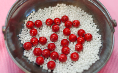 Red beads and white beads in a metal vase on a pink background