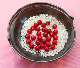 Red beads and white beads in a metal vase on a pink background