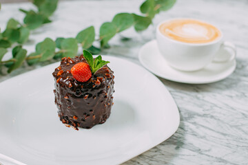 chocolate cake with nuts, strawberries and mint in a white plate on a marble table