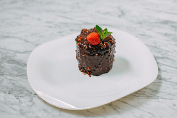 chocolate cake with nuts, strawberries and mint in a white plate on a marble table