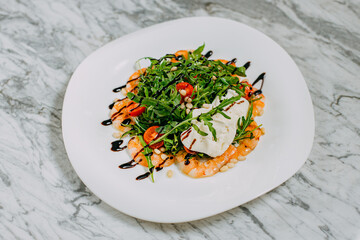 salad with shrimp, cheese and arugula in a white plate on a marble table