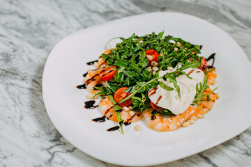 salad with shrimp, cheese and arugula in a white plate on a marble table