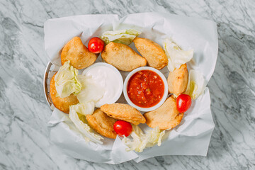 meat pasties with sauce and vegetables on a marble table
