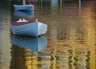 Two small boats floating in a pond with golden reflections in the water at twilight