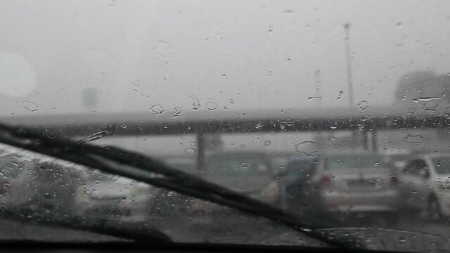 Raindrops on the windshield swipe by car swiper during heavy rain on traffic. 