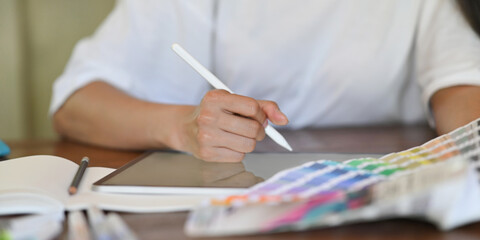 Cropped image of a woman's hands is drawing on a computer tablet that putting on a wooden workspace.