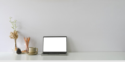Comfortable workspace is surrounding by a white blank screen computer laptop and accessories.