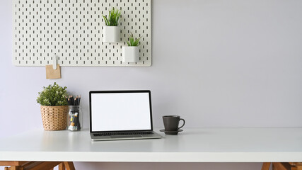 A white blank screen computer laptop is putting on a white workspace surrounded by office equipment.