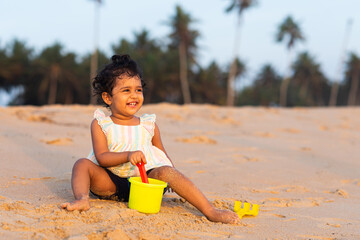 Playful Pretty Indian girl child/infant/toddler playing in the sand with her sand castle kit. Kid giving joyful expressions and playing on the beach.