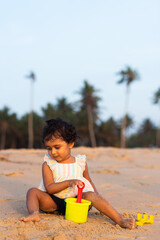 Playful Pretty Indian girl child/infant/toddler playing in the sand with her sand castle kit. Kid giving joyful expressions and playing on the beach.