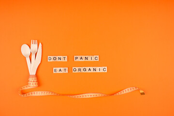 Diet and healthy eating concept - wooden cutlery, yellow measuring tape and words DONT PANIC EAT ORGANIC on wooden bricks, on bright orange background with copyspace. Healthy and sustainable lifestyle