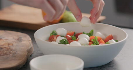 man add mozzarella into salad with kale and tomatoes in white bowl on kitchen countertop