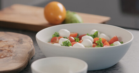 add mozzarella into salad with kale and tomatoes in white bowl on kitchen countertop