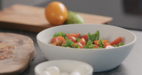 add tomato into salad with kale and in white bowl on kitchen countertop