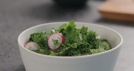 salting fresh salad with radish, cucumber and herbs in white bowl