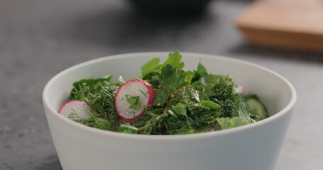 seasoning fresh salad with radish, cucumber and herbs in white bowl