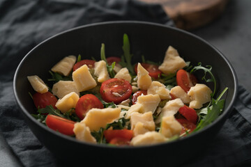 Fresh salad with cherry tomatoes, arugula and hard vintage cheese in black bowl on linen napkin