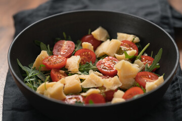 Fresh salad with cherry tomatoes, arugula and hard vintage cheese in black bowl on linen napkin