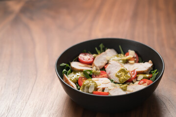 Salad with chicken, tomatoes and arugula in black bowl on walnut wood background with copy space