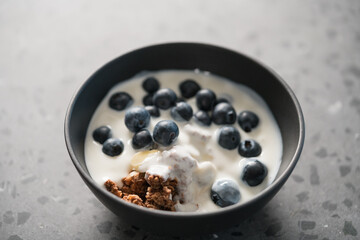 chocolate granola with fresh blueberries ang greek yogurt in black bowl on concrete background