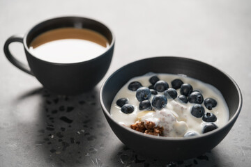 chocolate granola with fresh blueberries ang greek yogurt in black bowl and cup of coffee on concrete background