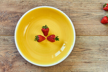 three strawberries on a yellow plate on a wooden tabletop