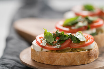 Bruschetta with mozzarella, tomatoes and basil with pesto on olive wood board