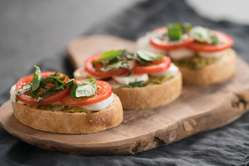 Bruschetta with mozzarella, tomatoes and basil with pesto on olive wood board