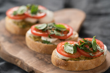 Bruschetta with mozzarella, tomatoes and basil with pesto on olive wood board