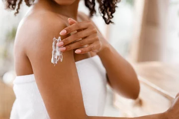 Poster Black woman applying moisturizing body lotion on skin after shower © Prostock-studio