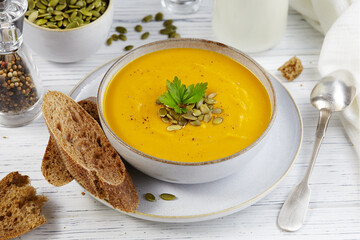 Pumpkin soup puree with seeds, greenery and dark pumpkin seed oil in the white bowl on a white background.