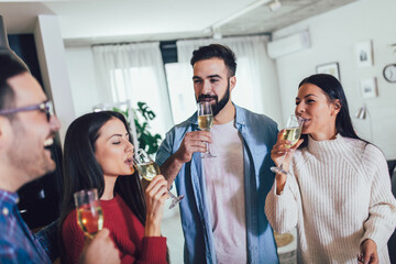 Young people cheering with champagne flutes and looking happy while having home party.