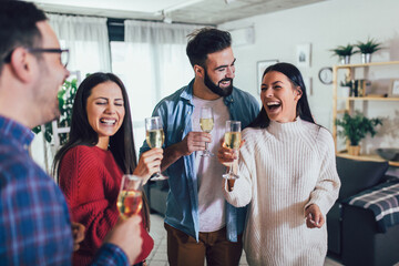 Young people cheering with champagne flutes and looking happy while having home party.