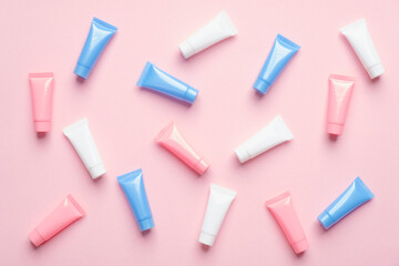 Many colorful cosmetic tubes on pink background. Blank plastic beauty products packaging. Flat lay,...