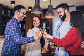 Young people cheering with champagne flutes and looking happy while having home party.