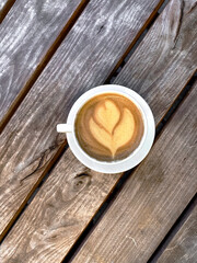 White cup of cappuccino with latte art on dark wooden background with copyspace fo text. Beautiful foam and stylish toning, selective focus
