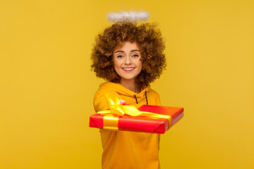 Happy holidays! Portrait of generous kind curly-haired angelic woman with saint nimbus giving...