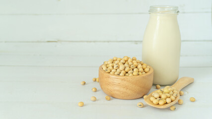 Soy milk in a bottle with soybeans in a wooden blow and scoop on white wood background with copy space. Alternative milk concept.