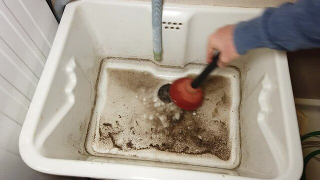 man tries to break through the clogged sink in the bathroom using a plunger. Clogged Drain Water in the Bathroom