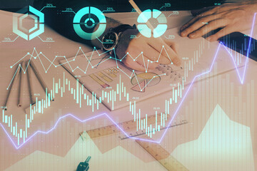 Double exposure of man's hands writing notes of stock market with forex chart.