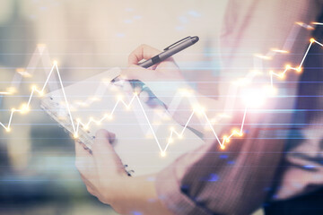 Multi exposure of hands making notes with forex chart huds. Stock market concept.