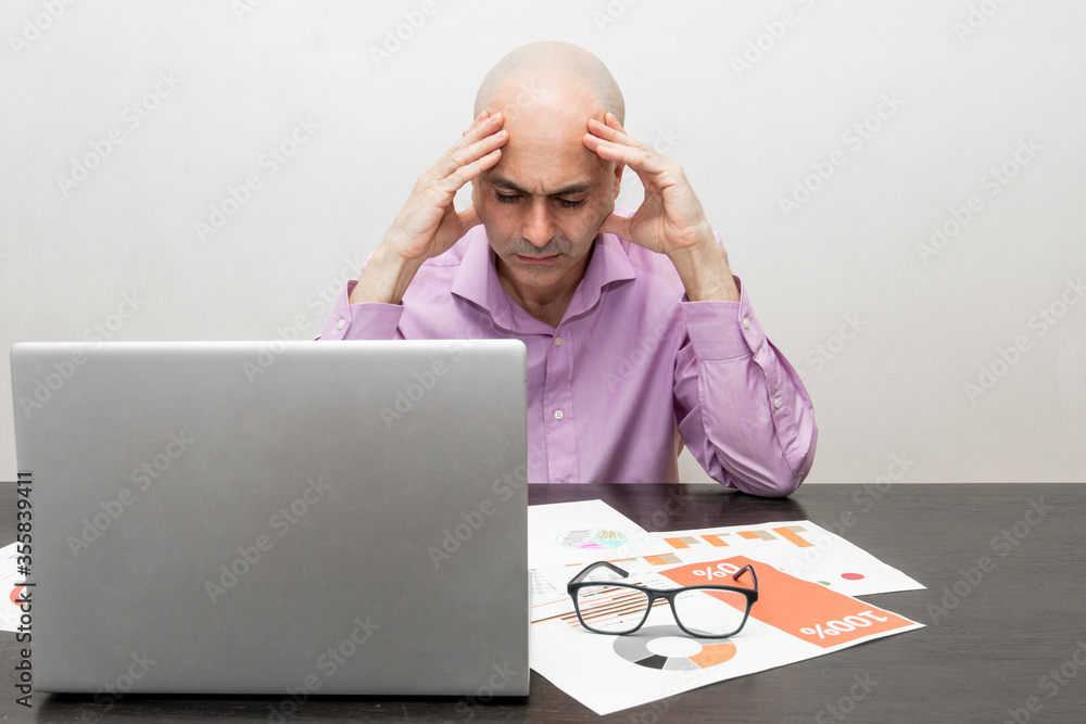 Poster man working with a laptop, papers with graphics and glasses with a thoughtful expression gesturing w