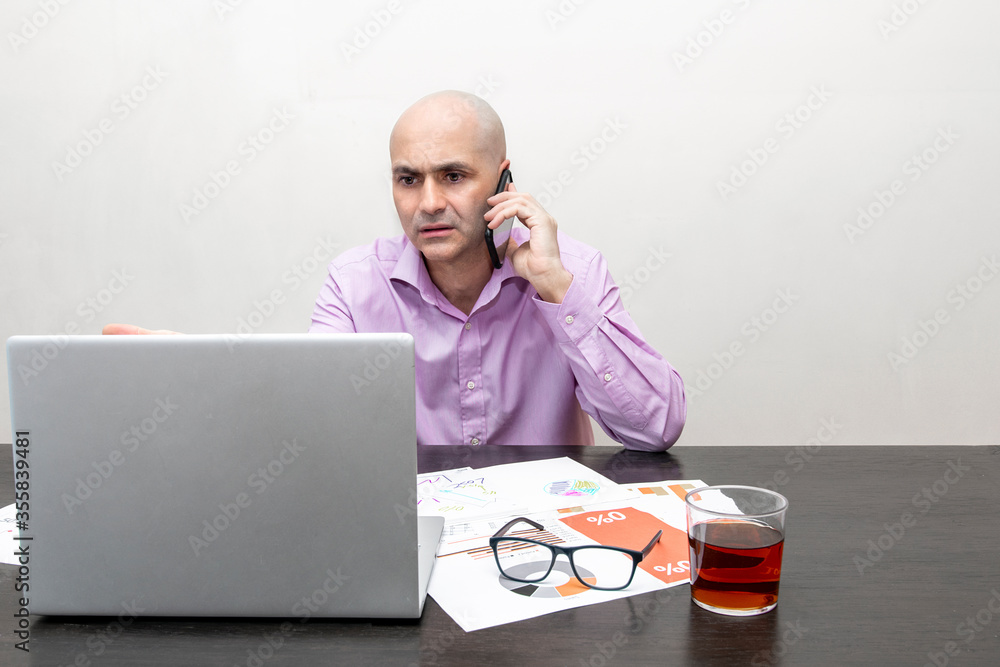 Fototapete man talking with a mobile while is working with a laptop and papers with graphics with a worried exp