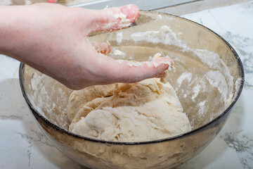 Thick dough is manually mixed in a transparent bowl.