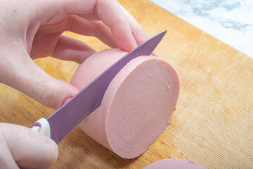 Close-up - hands cut soft pink sausage with a knife