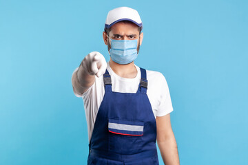 Fototapeta na wymiar Hey you! Portrait of strict handyman in overalls, mask and cap pointing finger to camera. Profession of service , post and delivery, engineer builder job. Expert repairman in workwear making choice