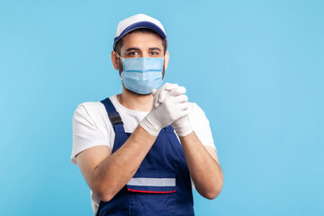 Fototapeta na wymiar Optimistic worker in overalls, mask and gloves keeping hands together in connection and agreement gesture. Profession of service industry, courier delivery, housekeeping maintenance. indoor isolated