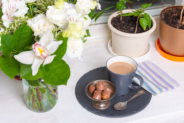 Bouquet with white orchids and a cup of coffee with milk, latte and sweets, top view, selective focus - holiday in a sweet home