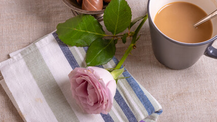 A large cup of coffee on the table, a spoon and a pink rose on a kitchen towel - congratulations for those in your sweet home