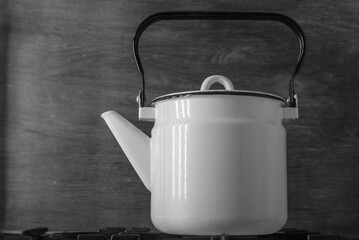 White enameled vintage teapot stands on a stove, on a black background - closeup